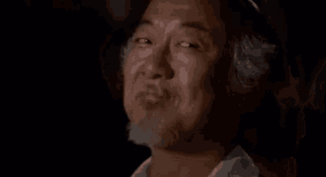 a man with a beard is smiling in a dark room with another man in the background .