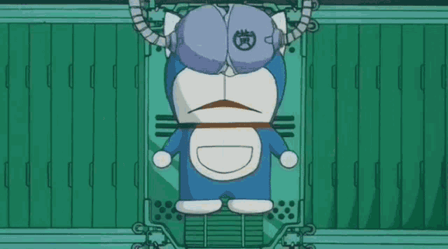 a cartoon character named doraemon is sitting in front of a green wall with a yellow object in his mouth .