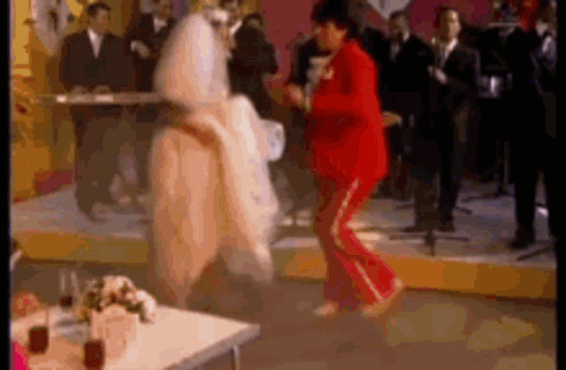 a bride and groom are dancing on a stage while a man in a red suit stands behind them .