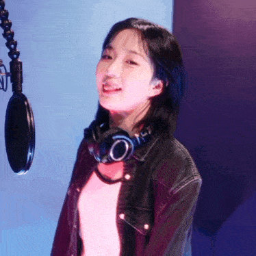 a young woman wearing headphones and a denim jacket is singing into a microphone