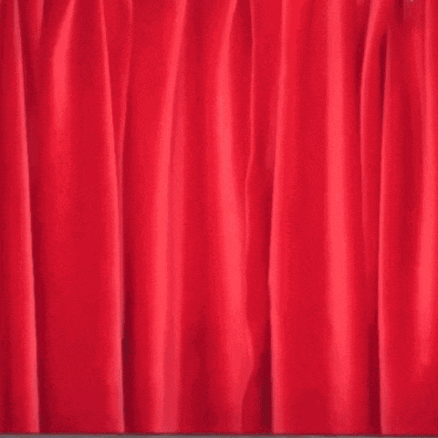 a man is peeking out from behind a red curtain and looking at the camera .
