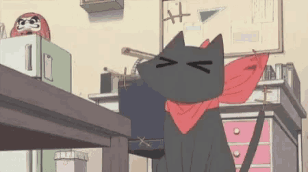 a black cat with a red scarf around its neck is sitting on a desk in a room .