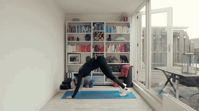 a woman is doing a yoga pose on a blue mat in front of a bookshelf