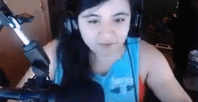 a woman is sitting in front of a microphone wearing headphones and a blue tank top .