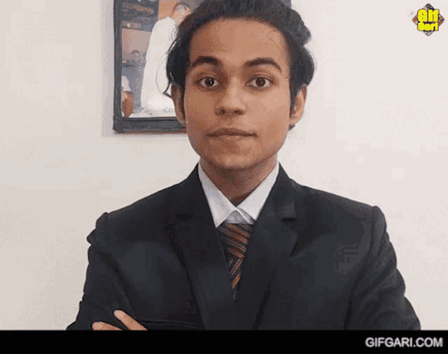a man in a suit and tie stands with his arms crossed in front of a picture that says gif gari