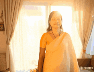 a woman in a yellow sari is standing in front of a window with the word minimx below her