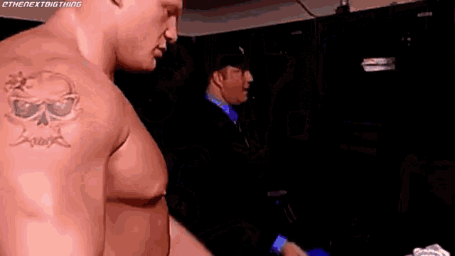 a man with a tattoo of a skull on his shoulder is standing in a locker room .