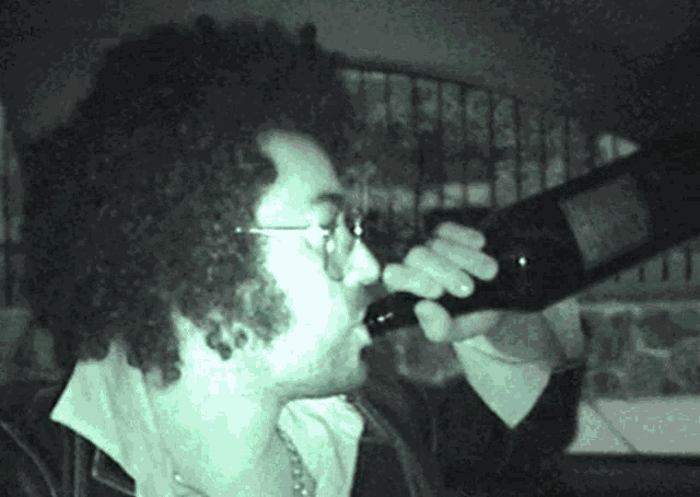 a man with curly hair is drinking from a wine bottle