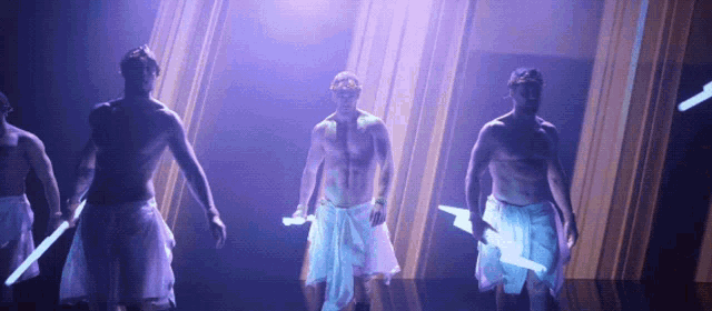 a group of men without shirts are standing on a stage holding glowing sticks