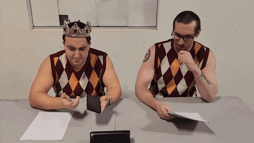 two men sitting at a table with one wearing a crown and the other wearing glasses