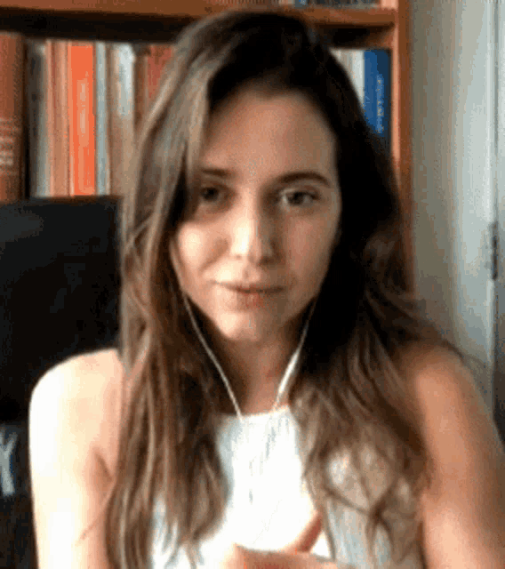 a woman wearing headphones looks at the camera in front of a bookshelf with books on it
