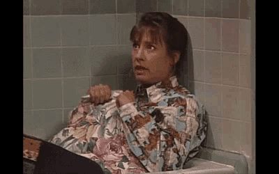 a woman in a floral shirt is sitting in a bathroom sink .