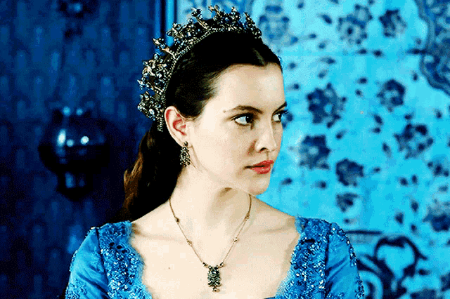 a woman wearing a blue dress and a necklace has a crown on her head