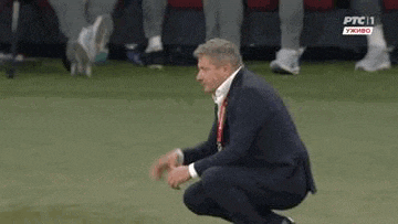 a man in a suit and tie is squatting on the grass on a soccer field .