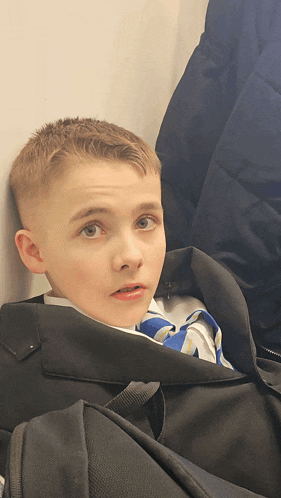 a young boy sitting in a black bag with a blue and white shirt on