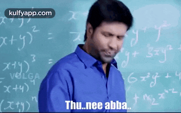 a man in a blue shirt is standing in front of a chalkboard with mathematical equations on it .