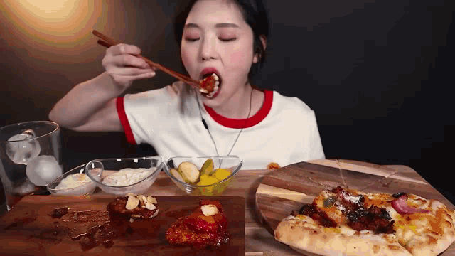 a woman is eating pizza with chopsticks and a bowl of pickles
