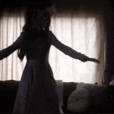 a woman in a white dress is standing in front of a window with her arms outstretched