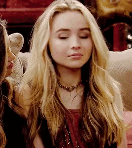 a woman with long blonde hair is sitting on a couch with her eyes closed and a necklace around her neck .
