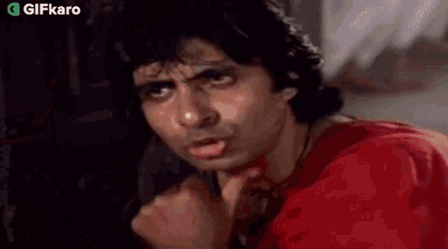 a man in a red shirt is talking on a phone and making a funny face .