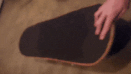 a person is pointing at a skateboard that is laying on the floor