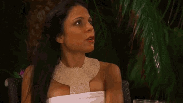 a woman in a white dress is sitting in front of a palm tree with her hands in the air .
