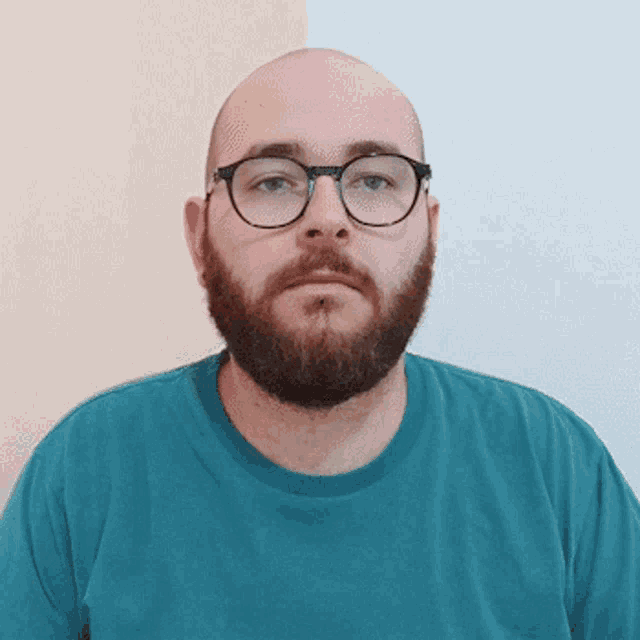 a bald man with glasses and a beard wears a blue shirt