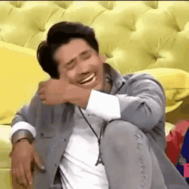 a man is sitting on a yellow couch laughing with his eyes closed .