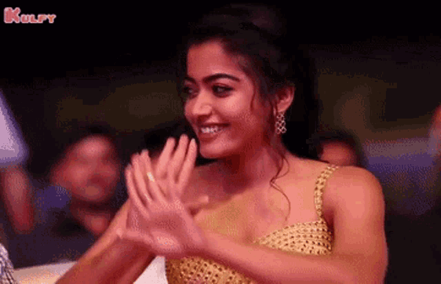 a woman in a gold dress is clapping her hands while smiling .