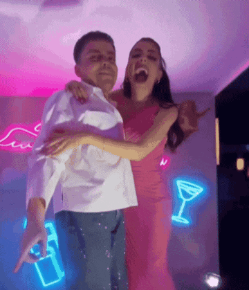 a man and a woman are dancing in a room with neon signs on the wall