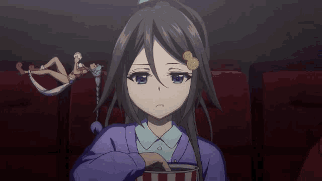 a girl in a purple sweater is holding a popcorn bucket while watching a movie
