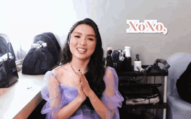 a woman in a purple dress is smiling in front of a xoxo sign
