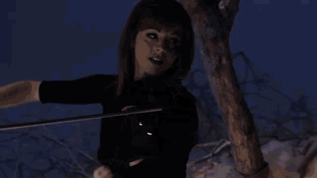 a woman is playing a violin while sitting next to a tree .