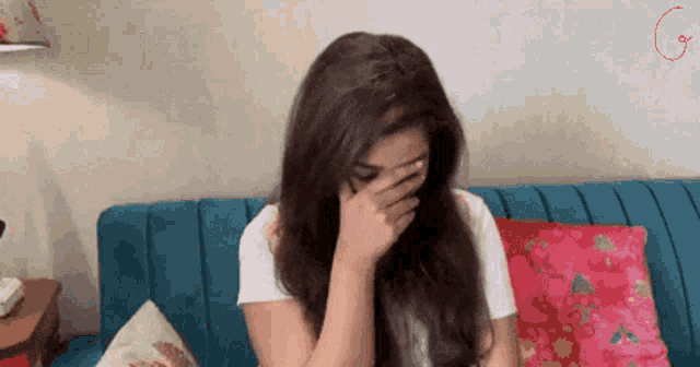 a woman is covering her face with her hand while sitting on a couch