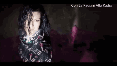 a woman with curly hair is wrapped in a scarf and standing in a dark room .