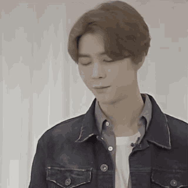 a man wearing a denim jacket and a white shirt is standing in front of a white curtain .