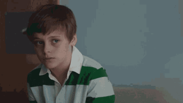 a young boy in a green and white striped shirt looks at the camera