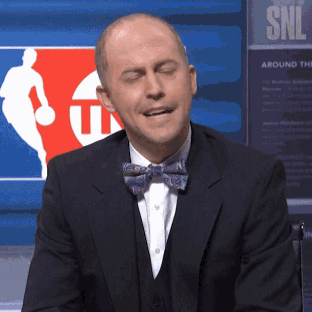 a man in a suit and bow tie is sitting in front of a sign that says snl