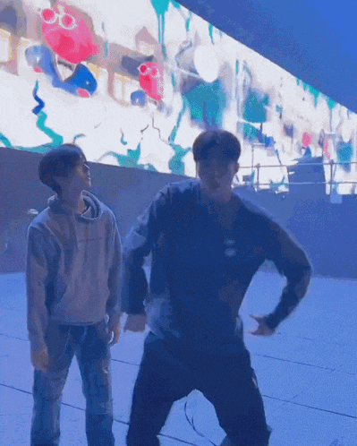 two men are dancing in front of a large screen which has a cartoon on it