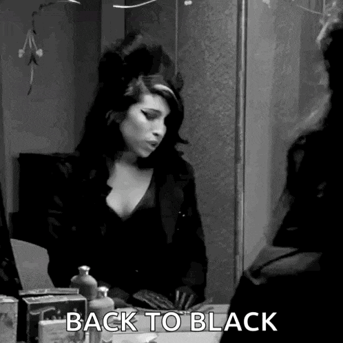 a black and white photo of a woman looking at herself in a mirror and saying `` back to black '' .