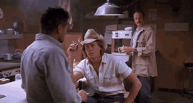 a man wearing a cowboy hat is smoking a cigarette in a kitchen