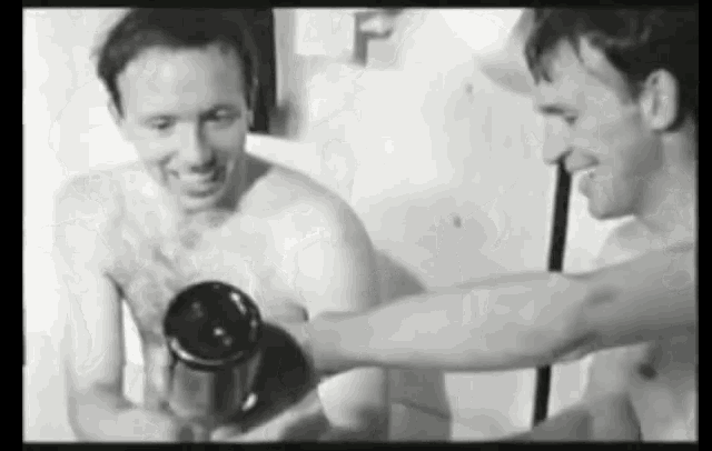 a black and white photo of two shirtless men drinking