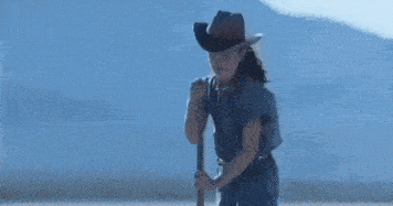 a man in a cowboy hat is kneeling down on the ground .