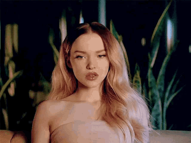 a woman in a strapless dress is sitting on a couch with her lips closed .
