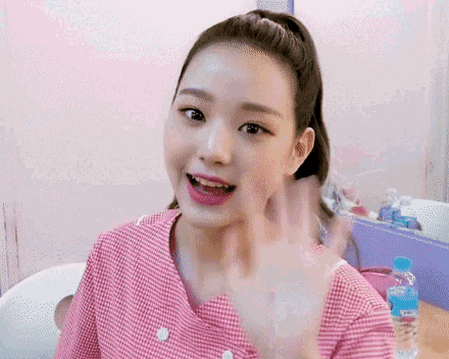 a girl in a pink shirt is waving her hand in front of a bottle of aquafina water
