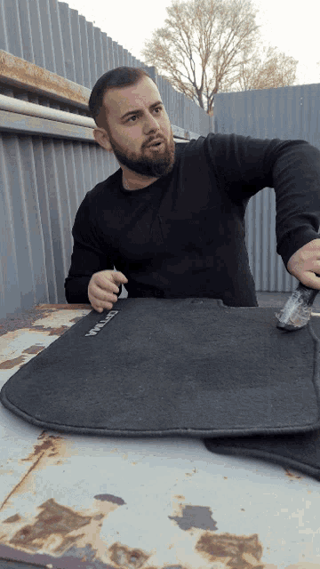 a man with a beard is sitting on a car mat with the word titan on it