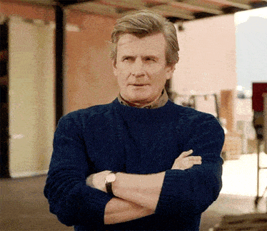 a man in a blue sweater has his arms crossed and is wearing a watch