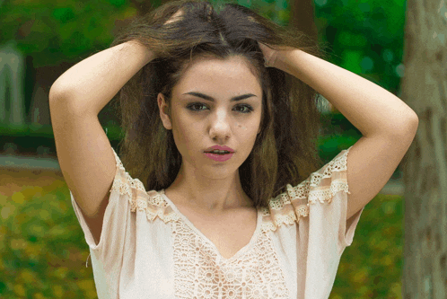 a woman in a white lace top is holding her hair
