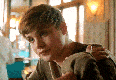 a young man sitting at a table with his hand on his shoulder looking at the camera