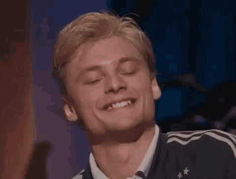 a man with blonde hair is smiling with his eyes closed and his teeth showing .